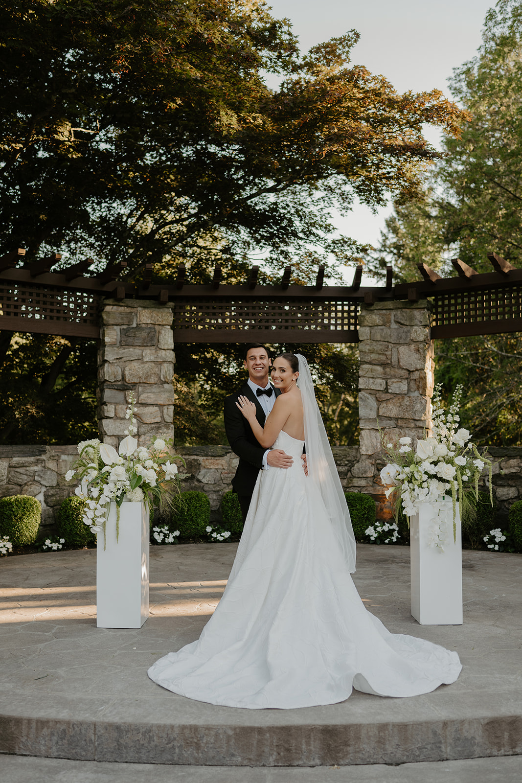 Bride and groom posing at the outdoor stone altar, smiling as the bride looks back over her shoulder.
